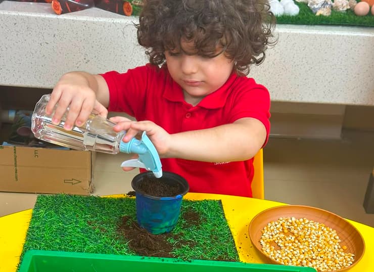 A child pouring water into a planting tray during a sensory activity at Little Regent